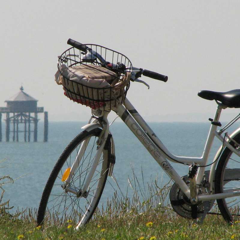 Vélo avec en arrière-plan la mer, un voilier et le phare du bout du monde près de La Rochelle aux portes du Marais poitevin